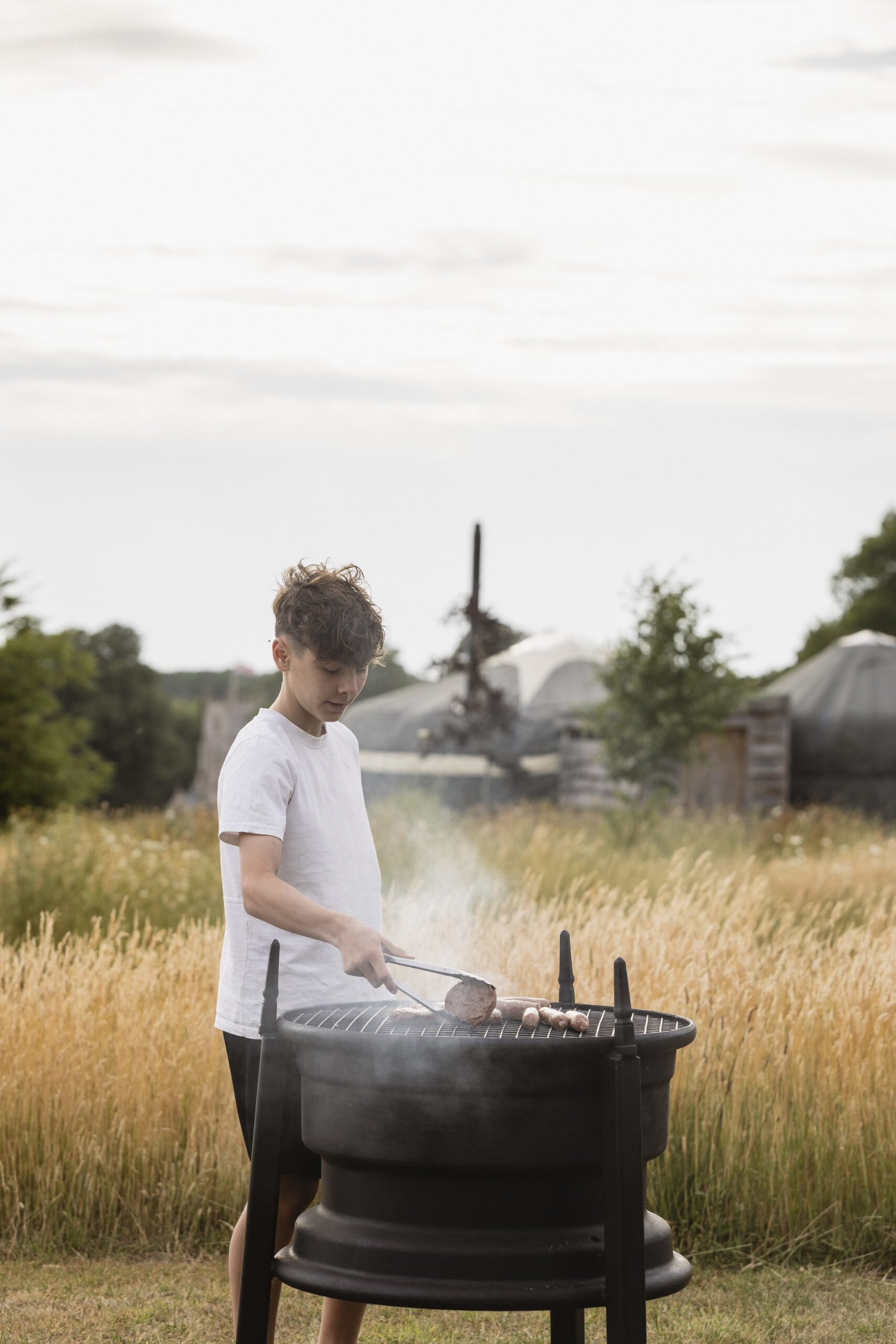 A child flips a burger on the BBQ at the Wild Meadow Glamping at Raynham